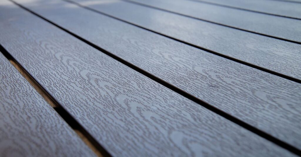 Close-up view of gray composite decking boards with a subtle wood grain texture, arranged in parallel lines outdoors. The surface appears clean and well-maintained.