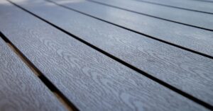 Close-up view of gray composite decking boards with a subtle wood grain texture, arranged in parallel lines outdoors. The surface appears clean and well-maintained.