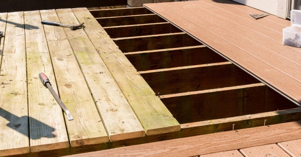 Partially finished deck with some old wooden boards and newly installed composite boards, tools like a hammer and pry bar visible, and open joists where boards are missing.